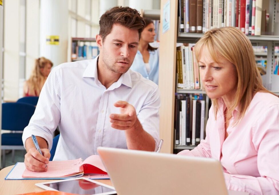 A man and woman sitting at a table looking at a laptop.